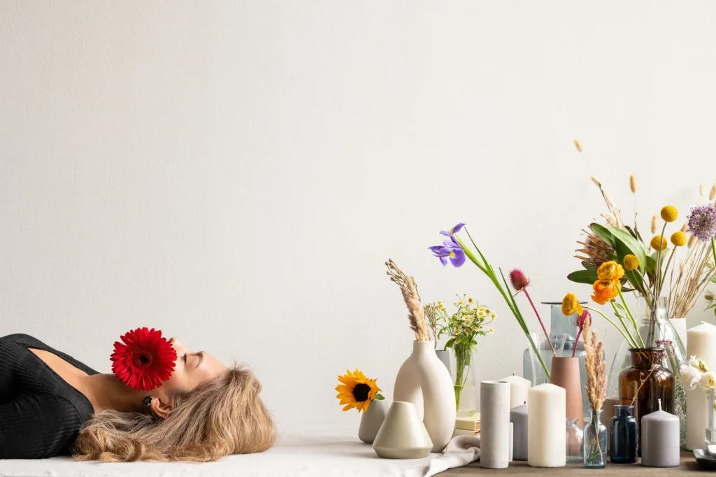 young serene woman with red herbera her mouth lying by variety fresh dried flowers wildflowers vases group candles 274679 10778